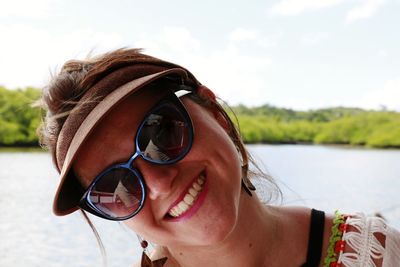 Close-up of happy woman wearing sunglasses against lake