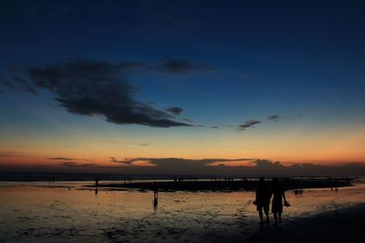 Silhouette people at beach against sky during sunset