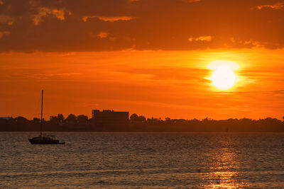 Silhouette sailboats in sea against orange sky