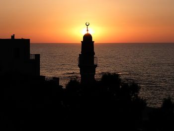 Silhouette building by sea against orange sky
