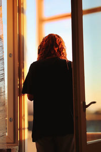 Rear view of young woman standing against door