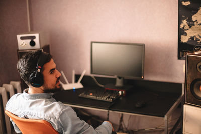 Young man in headphones sitting by desktop computer at home