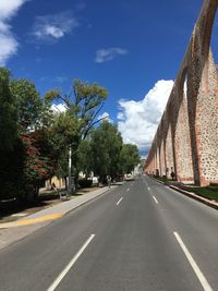 Road by trees against sky in city