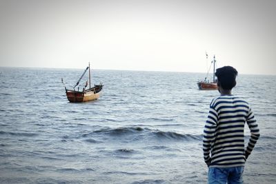 Rear view of man standing on boat in sea against clear sky