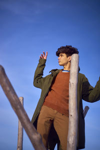 Young man looking away while standing by wooden posts against sky