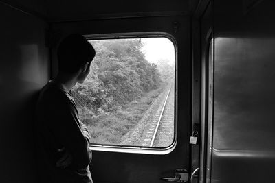 Rear view of man standing against window in train