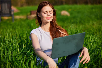 Portrait of young woman using laptop while sitting on grassy field