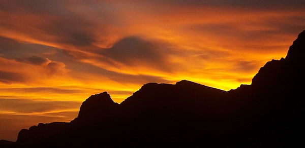 Low angle view of silhouette mountains against orange sky