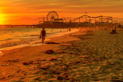 Ferris wheel on beach against sky during sunset