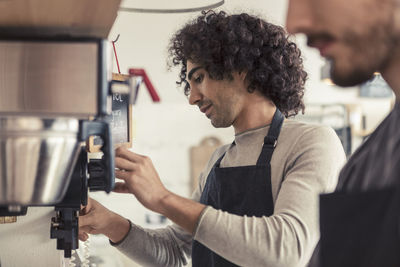 Male entrepreneur making coffee from machine while standing by coworker at cafe