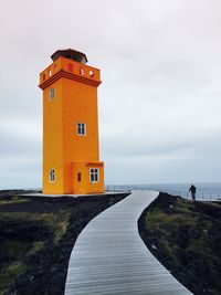 Boardwalk leading towards lighthouse against sky