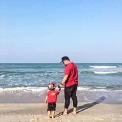 Rear view of mother with daughter on beach against sky