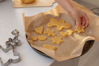 Children's hand lays dough figurines in the form of christmas symbols on parchment