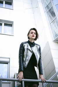 Portrait of young woman leaning on railing against building