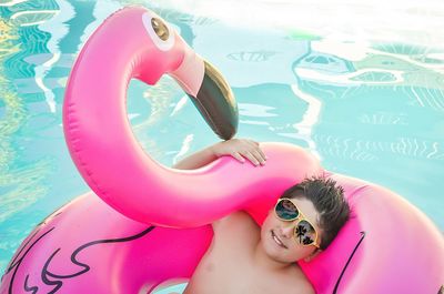 High angle portrait of boy floating on pink flamingo inflatable ring on pool