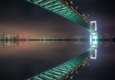 Illuminated buildings and bridge reflecting in lake at night