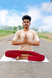 Young man sitting on cross against sky doing yoga