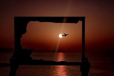 Silhouette street light by sea against sky during sunset