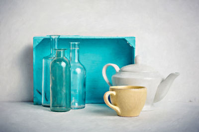 Close-up of teapot with cup by bottles on table