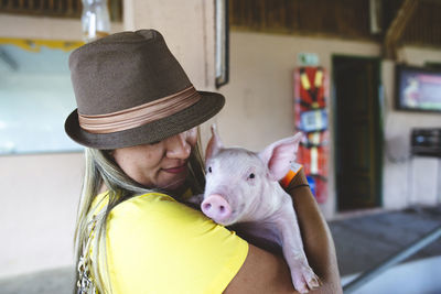 Smiling female standing in city near building and hugging adorable little pink pig