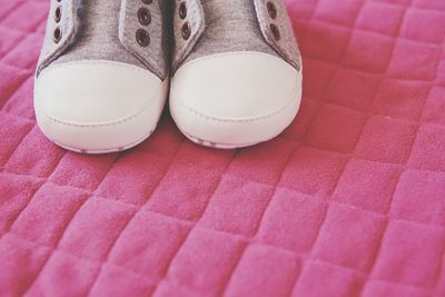Low section of kid shoes on pink background