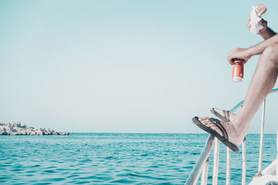 Low section of man sailing on sea against clear sky