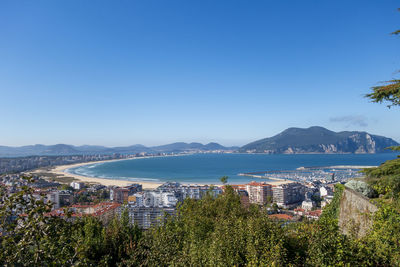 Aerial view of city by bay against clear blue sky