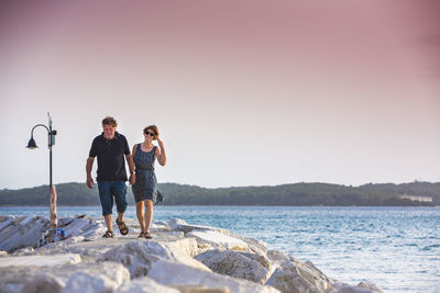 Full length of couple walking on pier by sea against clear sky