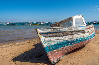 Boat moored on beach against blue sky