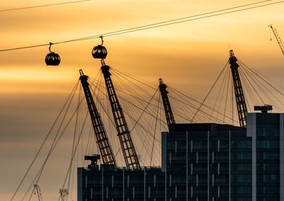 Cranes and overhead cable car against sky during sunset