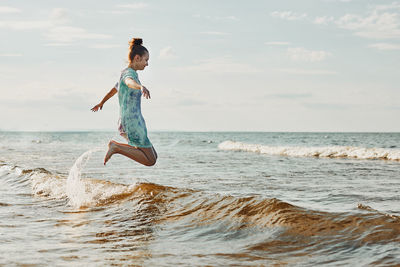 Girl enjoying sea jumping over waves spending a free time over sea on a beach at sunset