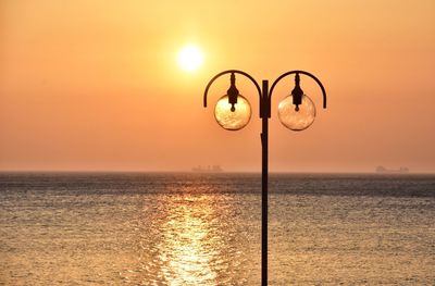 Street light by sea against sky during sunset