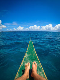 Low section of man sitting on boat in sea against blue sky