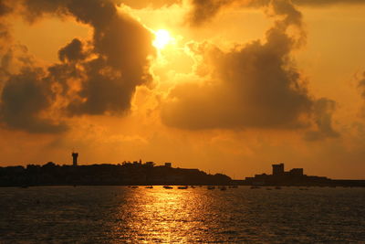 Silhouette city by sea against sky during sunset