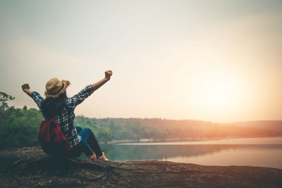 Man with arms raised against sky during sunset
