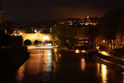 Illuminated city by river against sky at night