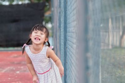 Portrait of cute girl standing by chainlink fence