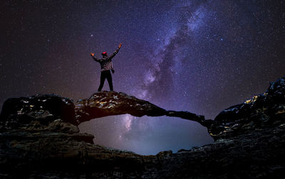 Rear view of man standing on rock against sky at night