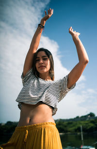 Young woman with arms raised standing against sky during sunset