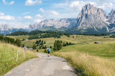 Rear view of man walking on road amidst mountains against sky