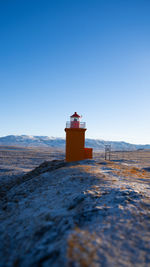 Lighthouse by sea against clear sky