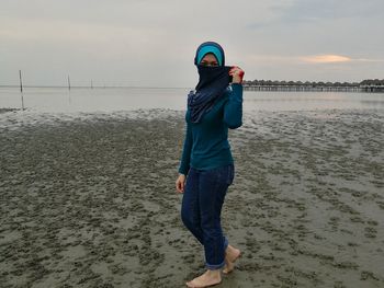Full length of woman with hijab standing at beach during dusk