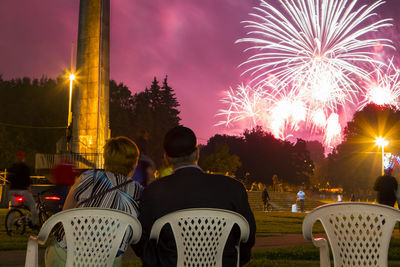 Rear view of man and woman watching firework display at night