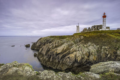 Lighthouse on rock by sea against sky