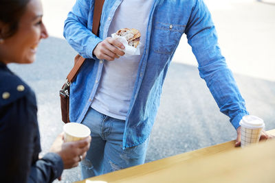 Midsection of young man having bread and coffee at food truck in city