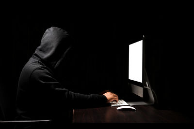 Computer hacker using computer against black background