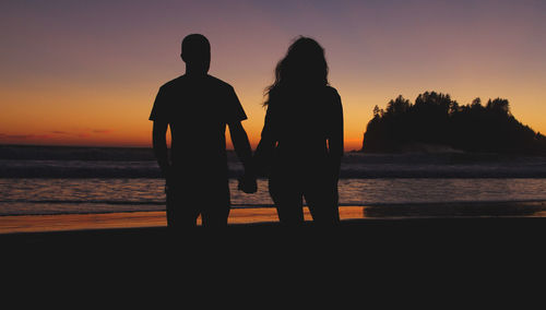Silhouette couple standing at beach during sunset