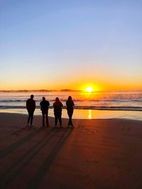 Silhouette people on beach against sky during sunset