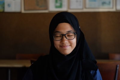 Close-up of happy girl wearing hijab and eyeglasses with closed eyes at restaurant