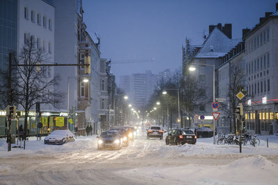 Cars on road by buildings in city at winter